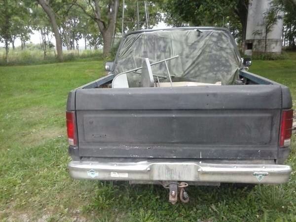 Dark gray pickup truck rear view, covered bed with camouflage tarp, parked on grass