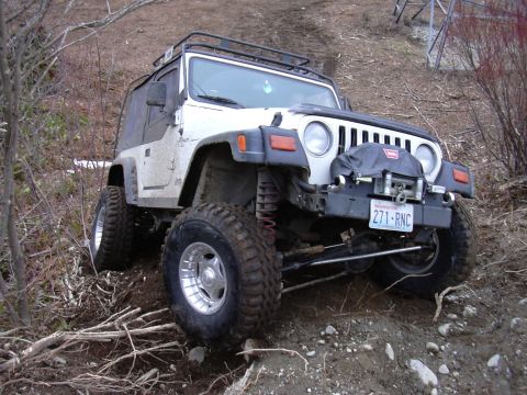 1991 Ford Bronco - A white Jeep Wrangler navigates a steep, muddy incline, equipped for off-road adventure.