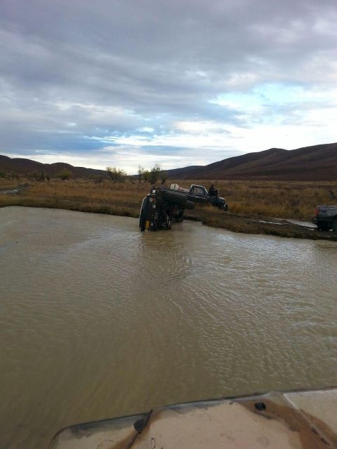 1990 Ford F-250 - Several trucks are stuck in a muddy body of water with hills in the background.