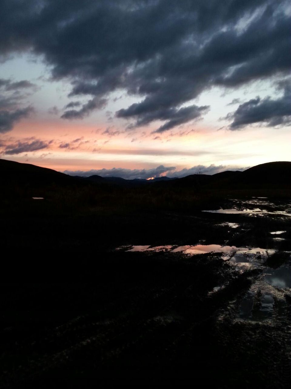 Dark landscape with puddles reflecting a colorful sunset sky