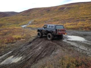 1990 Ford F-250 - Off-road vehicle navigates a challenging muddy trail in a remote, hilly area.