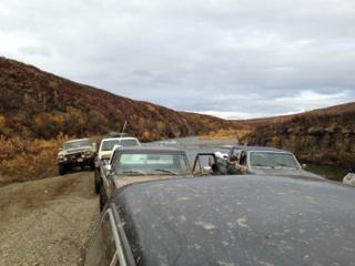 1990 Ford F-250 - Multiple trucks are lined up on a dirt road, with a river and hills visible in the background.