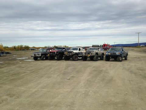 1990 Ford F-250 - Several modified trucks are lined up in an outdoor lot under a cloudy sky.