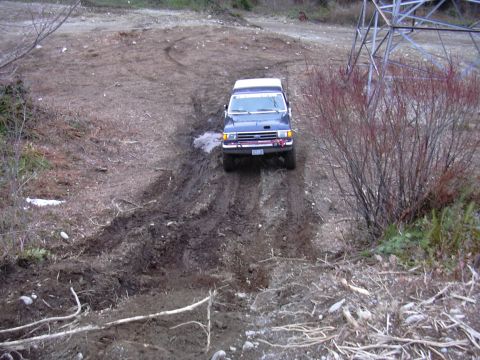 1991 Ford Bronco - A 1991 Ford Bronco navigates a challenging, muddy terrain with visible tire tracks.