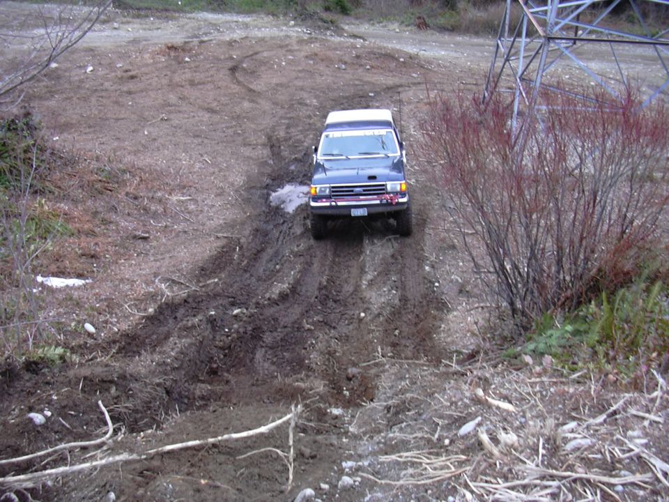 1991 Ford Bronco driving on a muddy, unpaved road