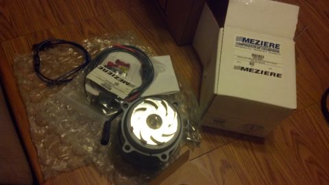 2003 Ford Crown Victoria - Meziere electric water pump with finned impeller, wiring harness and relay laid out beside its box on a wood floor.
