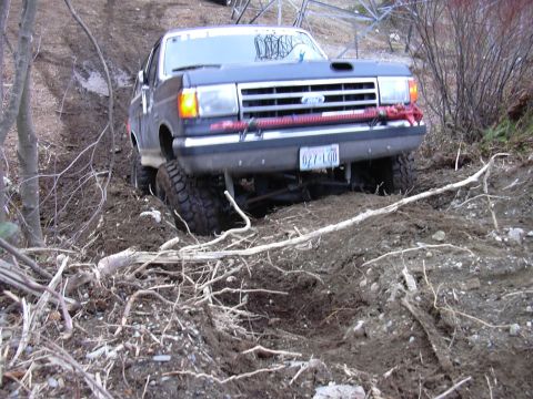 1991 Ford Bronco - A dark blue Ford F-Series truck navigates a muddy off-road trail.