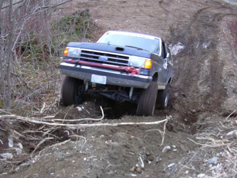 1991 Ford Bronco - A dark blue 1991 Ford Bronco navigates a challenging dirt incline, its large tires gripping the uneven terrain.