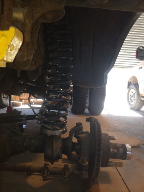 1996 Ford Bronco - Close-up view of a vehicle's front axle and suspension system, with another vehicle in the background.