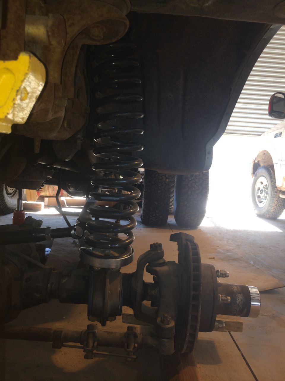 Front axle assembly with coil spring suspension, brake rotor, and hub. Another vehicle is partially visible in the background