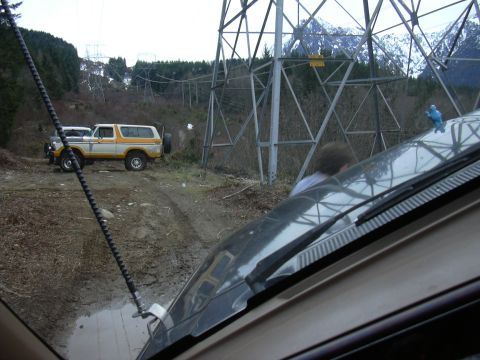 1991 Ford Bronco - A two-tone Ford Bronco is seen off-road near a large power line tower, with another vehicle partially visible in the foreground.