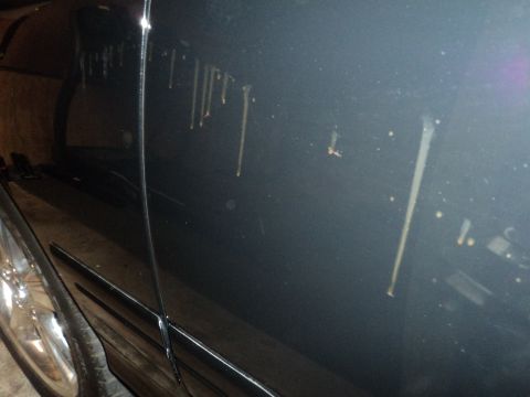 2004 Mercury Grand Marquis - Close-up of a dark car's side panel showing dirt streaks and a portion of a chrome wheel.