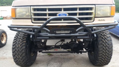 1988 Ford Bronco - The front view of a tan Ford Bronco modified with a heavy-duty bumper and off-road tires.