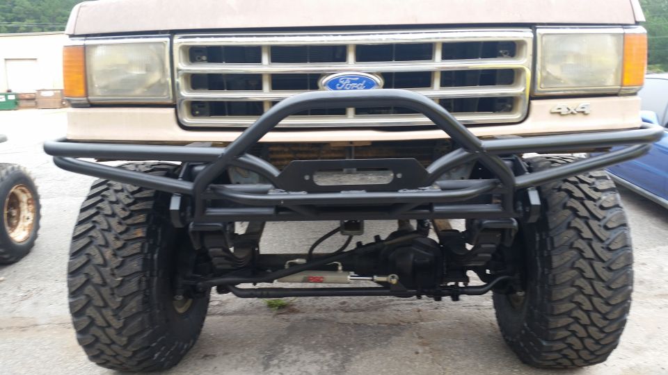 Tan 1987 Ford Bronco front end with a black winch bumper and large off-road tires