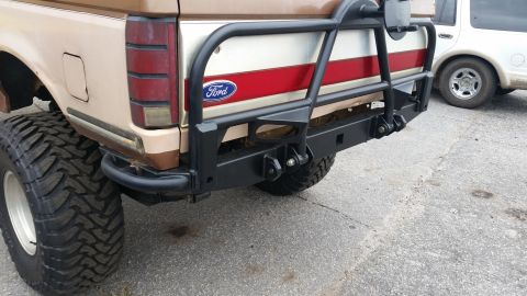 1988 Ford Bronco - Rear view of a 1988 Ford Bronco, modified with a heavy-duty bumper and spare tire mount, alongside another vehicle.