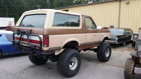 1988 Ford Bronco - This lifted Ford Bronco has a custom rear bumper and spare tire mount. Other vehicles are parked nearby.