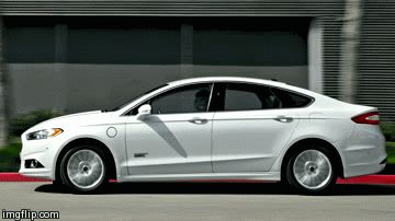 1993 Ford Taurus - A white sedan is captured in motion, passing by a building with a modern facade.