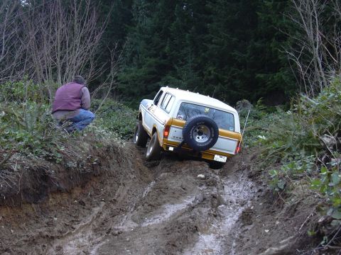 1991 Ford Bronco - A man watches a Ford Bronco navigate a steep, muddy incline in a wooded area.