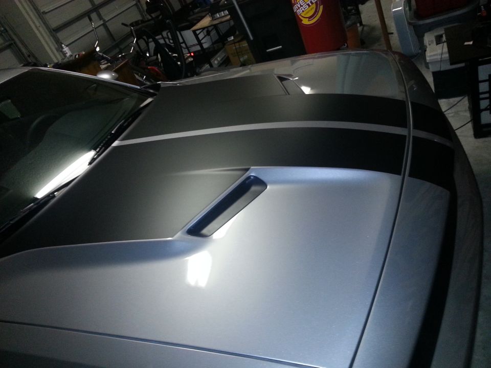 Silver car hood with black and gray racing stripes and a functional vent