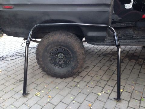 1979 Ford Bronco - A black roll cage is positioned in front of the wheel and open door of a dark-colored SUV.