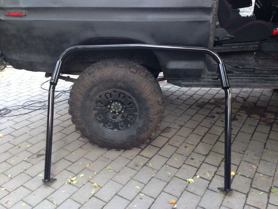 Black roll cage in front of a dark SUV's wheel and door