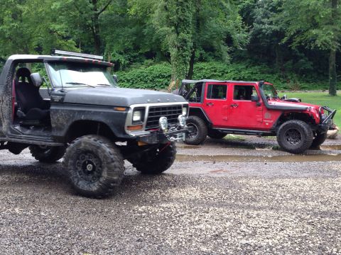 1979 Ford Bronco - A black 1978 Ford Bronco and a red Jeep are parked on a gravel surface with trees in the background.