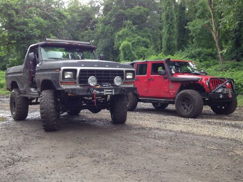 1979 Ford Bronco - A lifted black Ford Bronco from the late 1970s sits beside a red Jeep on a dirt road.
