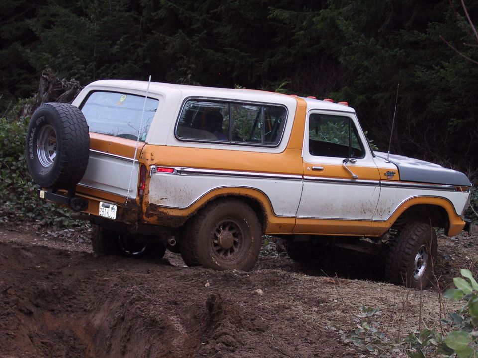 1978 Ford Bronco with orange and white paint on a dirt trail, spare tire mounted on the back