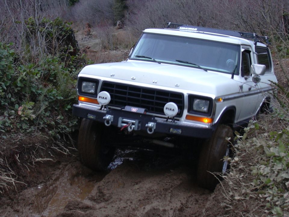 White Ford Bronco driving through a muddy trail with aftermarket bumper and winch