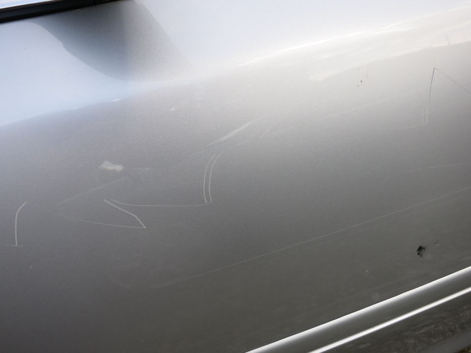 Silver car door with numerous white scratches and a small dark mark