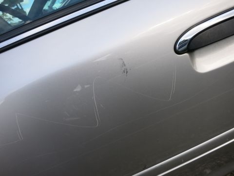 1991 Ford LTD Crown Victoria - Close-up of a beige car's side door panel showing extensive scratches and scuff marks.