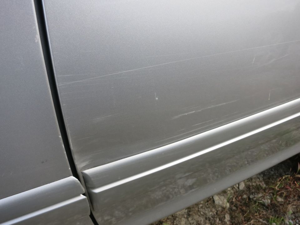 Silver car door and fender with numerous scratches and a body line
