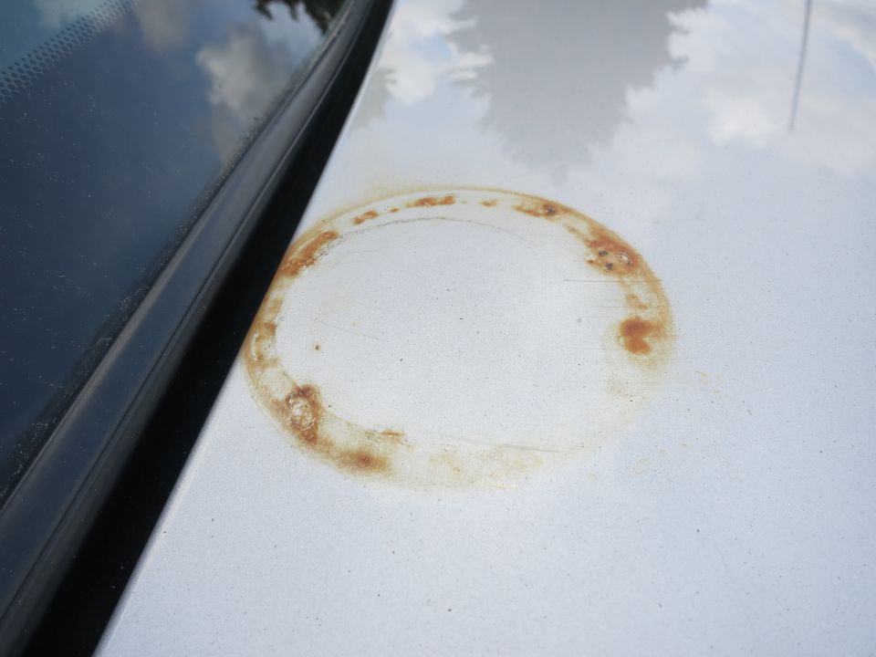Rust ring on a silver car hood near the windshield trim