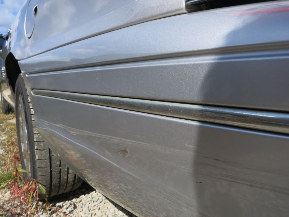 Close-up of a silver sedan's side panel showing a chrome trim strip and a tire