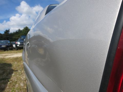 1991 Ford LTD Crown Victoria - Close-up of a silver car's rear quarter panel, with other vehicles parked in the background under a cloudy sky.