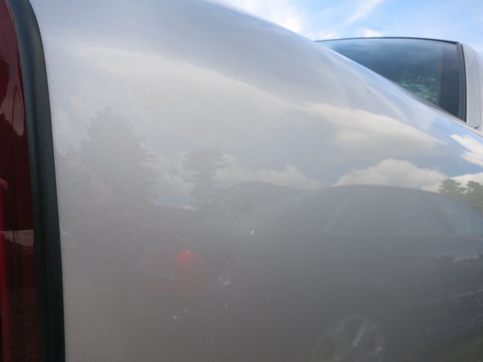 Silver car side panel with reflection of clouds and trees. Another vehicle is visible behind