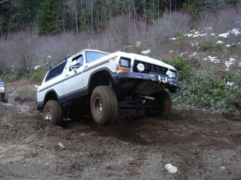 1991 Ford Bronco - A white Ford Bronco navigates a challenging muddy terrain, with another vehicle visible in the background.
