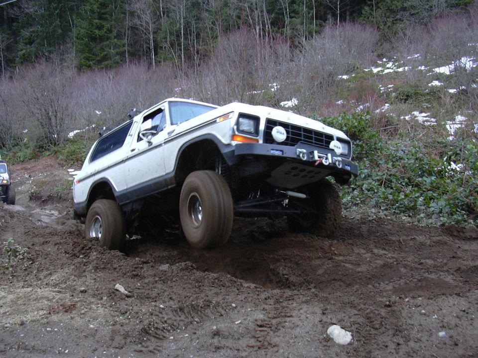 White 1978 Ford Bronco off-roading on a muddy hill