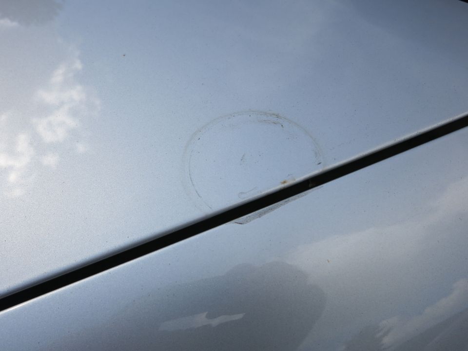 Silver car hood with a circular stain and a seam