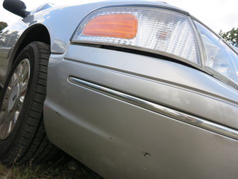 1991 Ford LTD Crown Victoria - Close-up of a silver sedan's front quarter panel and headlight assembly, showing chrome accents and a portion of the wheel.