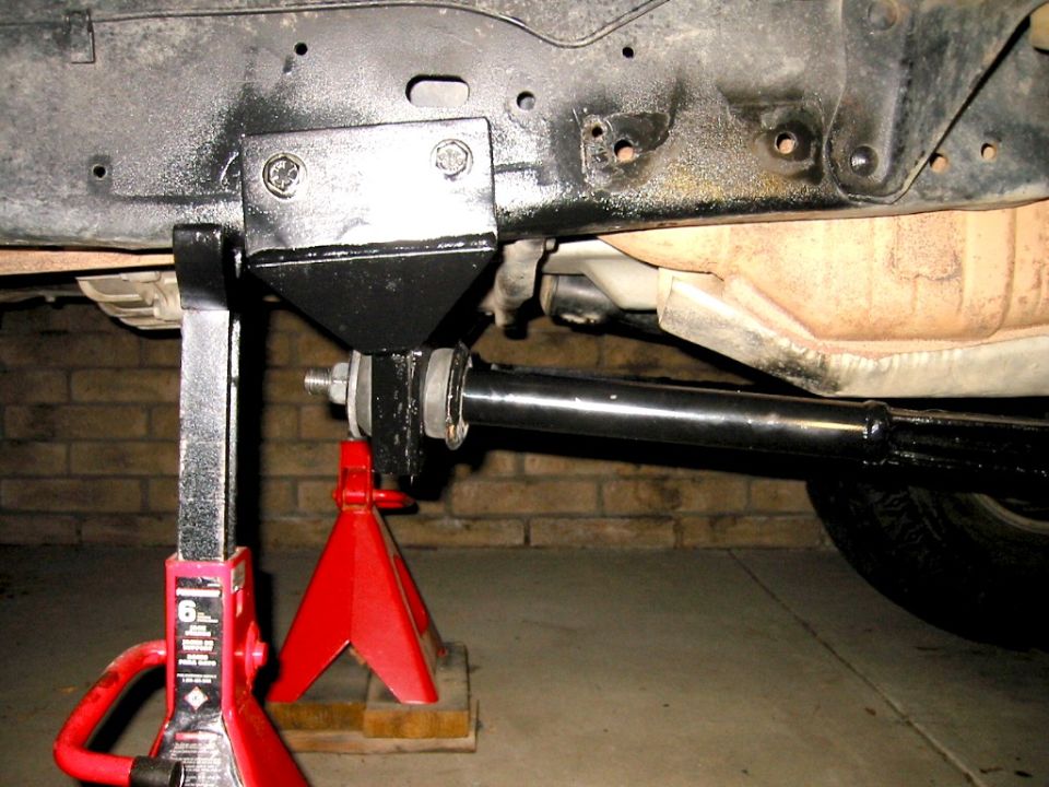 Vehicle underbody on red jack stand showing black frame bracket and suspension link