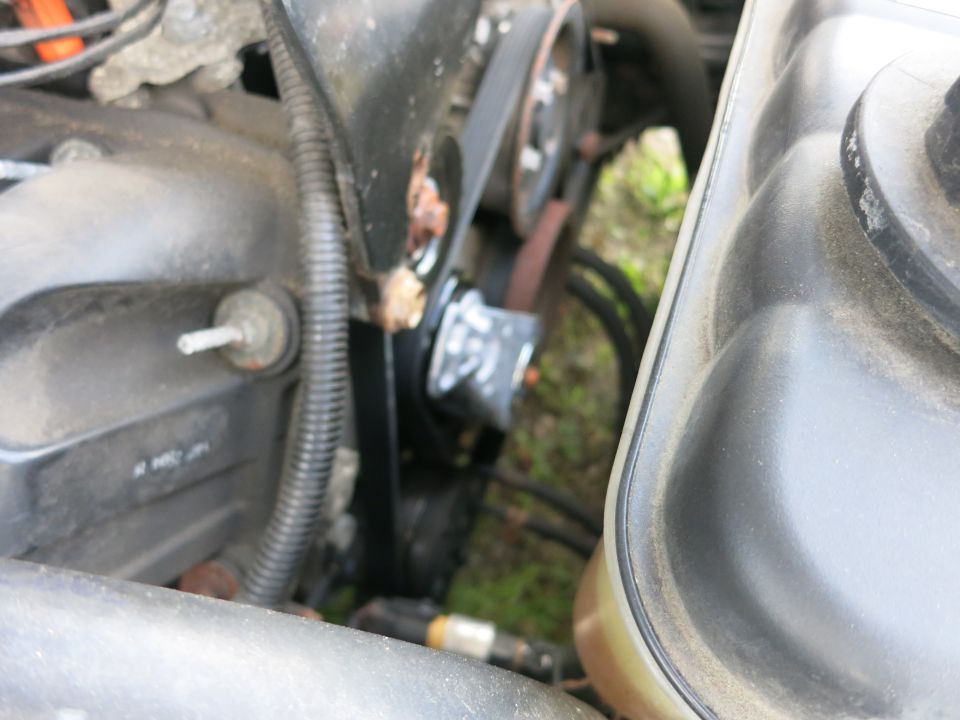 Close-up of engine components including a belt and pulley system, with a plastic reservoir visible on the right