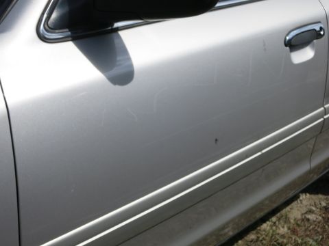 1991 Ford LTD Crown Victoria - Close-up of a silver car door showing numerous scratches and a chrome door handle.