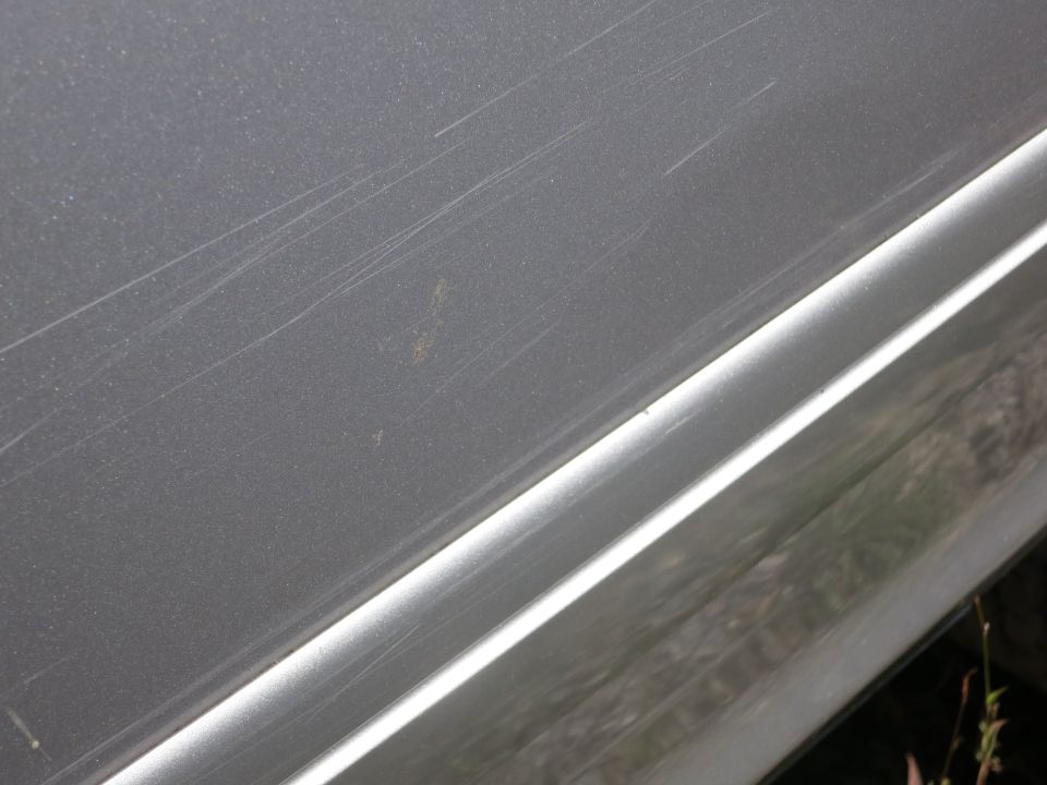 Silver car door panel with numerous scratches and a small rust spot