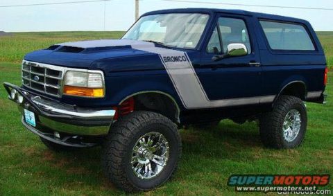1994 Ford Bronco - Blue 1994 Ford Bronco with custom hood scoop and silver stripe parked on grass.