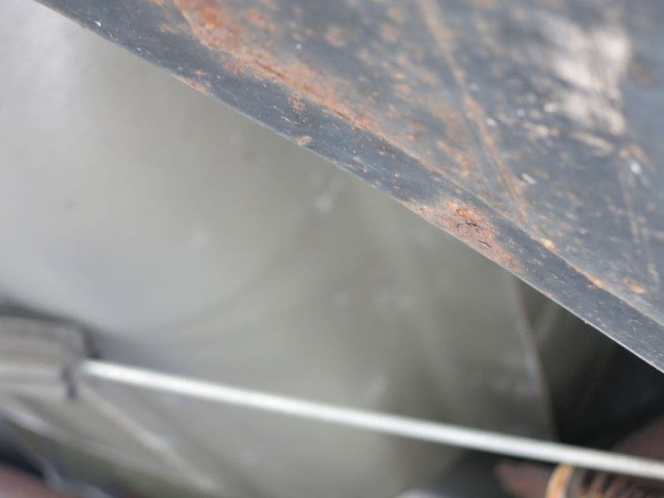 Underside of a vehicle with rust on a dark metal panel and a light-colored surface below