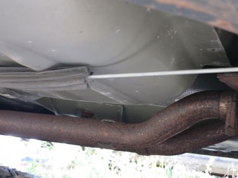 1991 Ford LTD Crown Victoria - The underside of a vehicle is visible, a rusty exhaust system and a fuel line running along the frame.