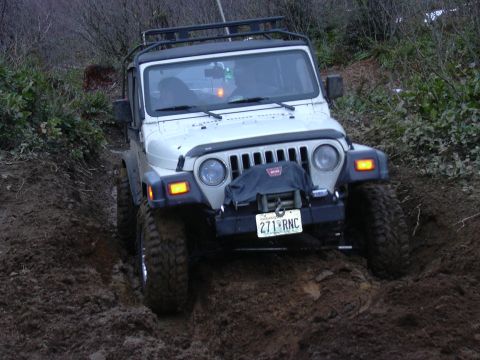 1991 Ford Bronco - A white Jeep Wrangler TJ navigates a muddy trail, equipped with a winch for off-road challenges.
