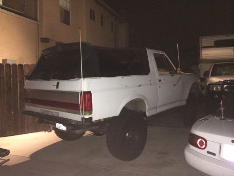 1990 Ford Bronco - White 1990 Ford Bronco with a soft top, lifted suspension, parked outdoors at night.