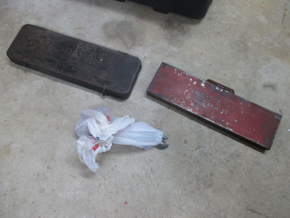 Two metal toolboxes and a plastic bag containing tools on a concrete floor